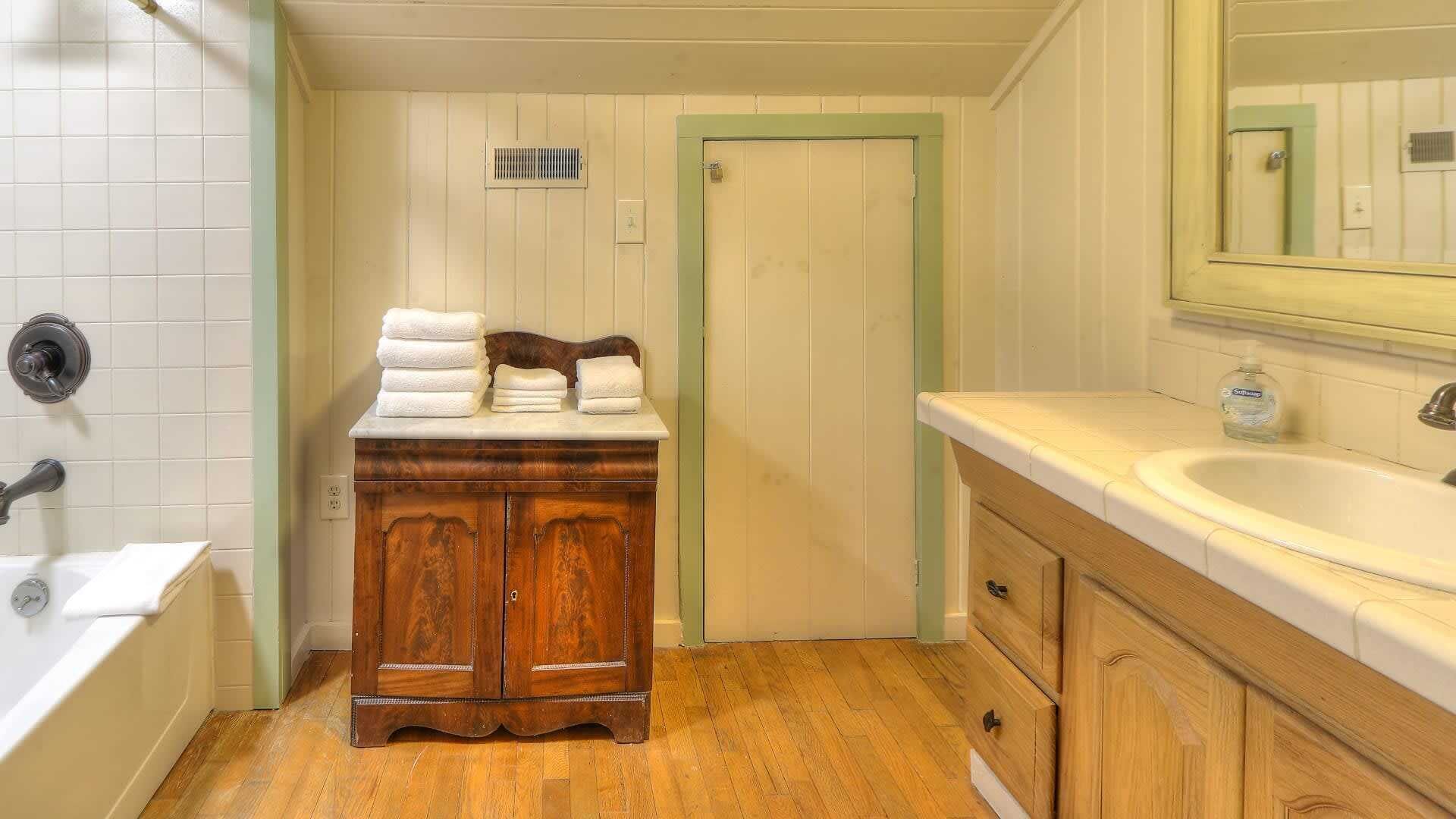 Une salle de bain avec un meuble-lavabo en bois, un lavabo blanc, un miroir et une porte.