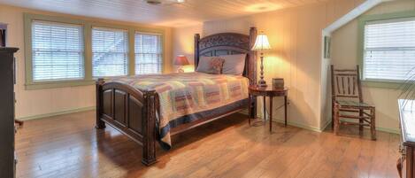A bedroom with a wooden bed, a nightstand, a lamp, a chair, and a window with blinds.