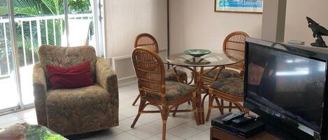 Una sala de estar con televisor, una mesa de comedor con sillas, un sofá y un ventilador de techo.