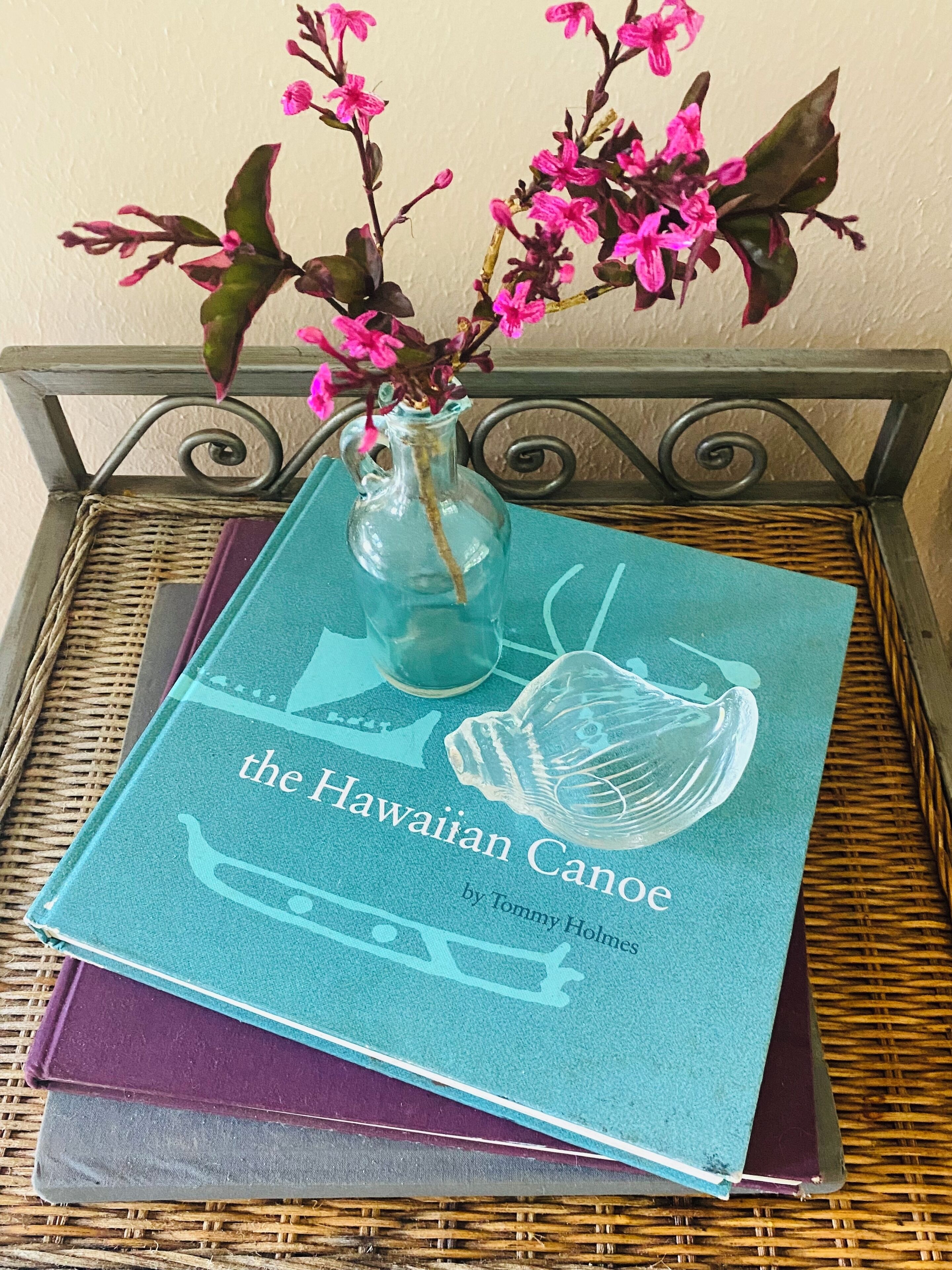 Un libro intitolato "the Hawaiian Canoe" di Tommy Holmes su un tavolino di vimini.