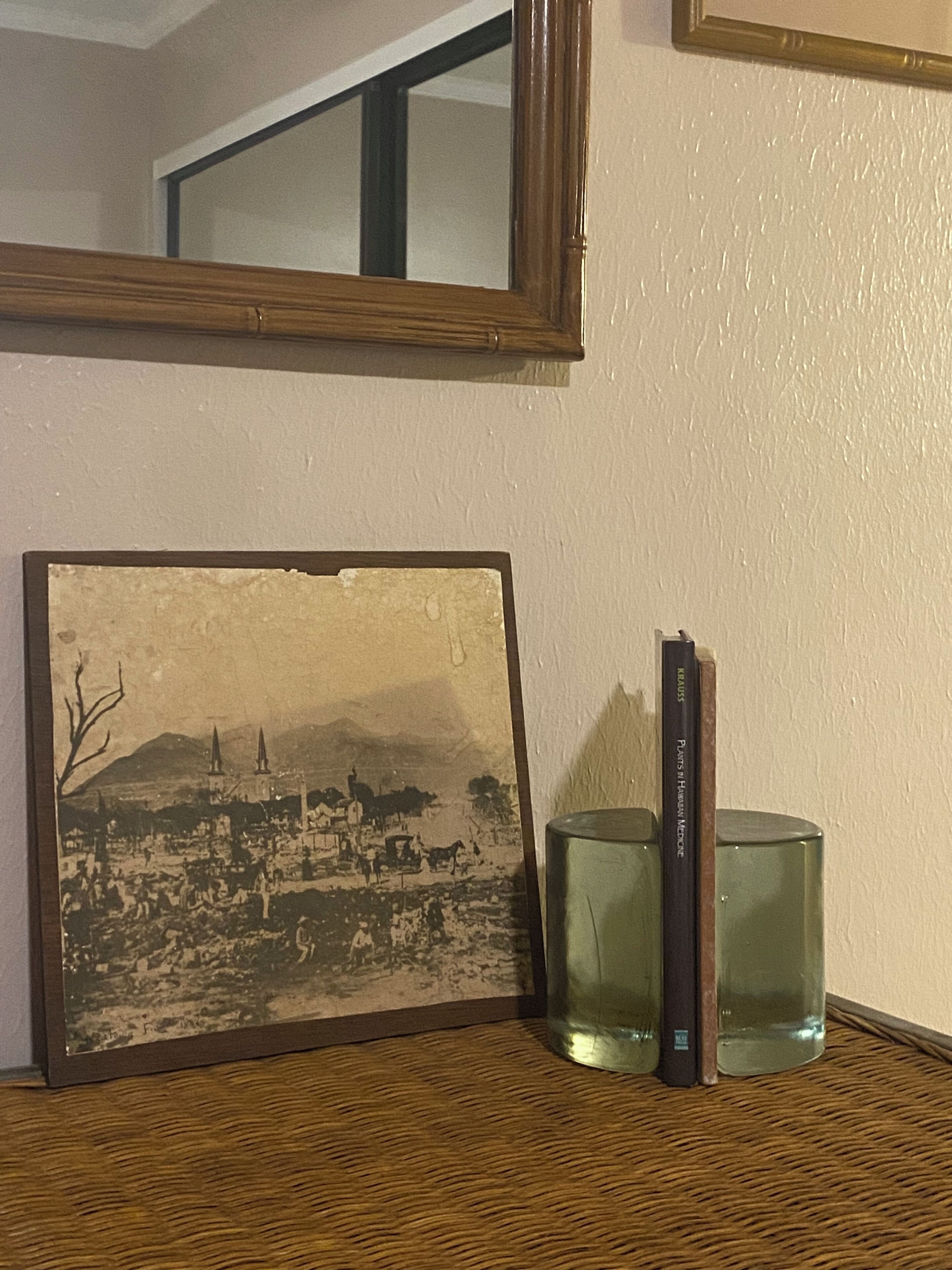 A framed historical photograph, a book, and two clear glass vases on a woven shelf.