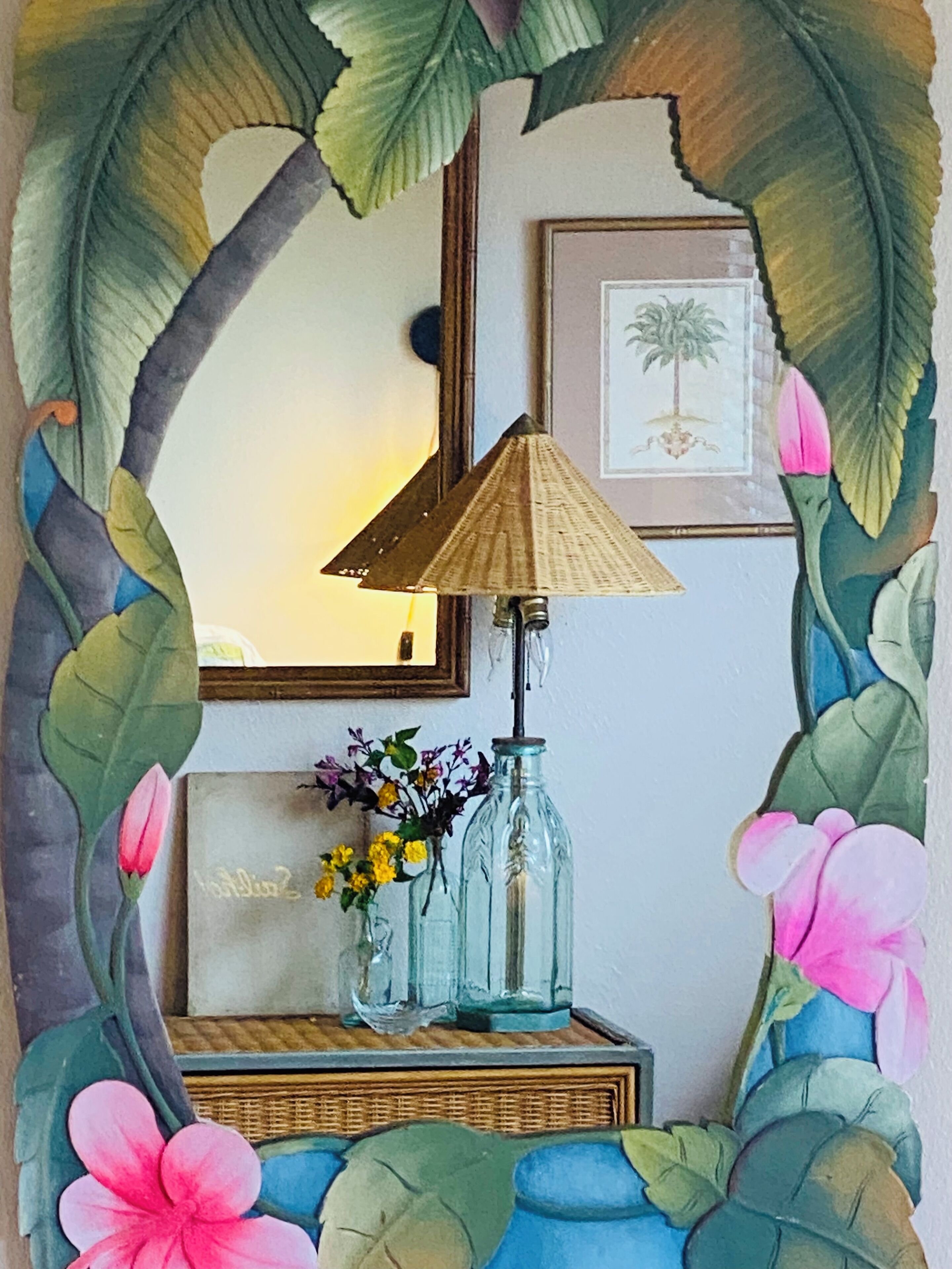 A mirror with a decorative frame, a lamp, and a vase with flowers.