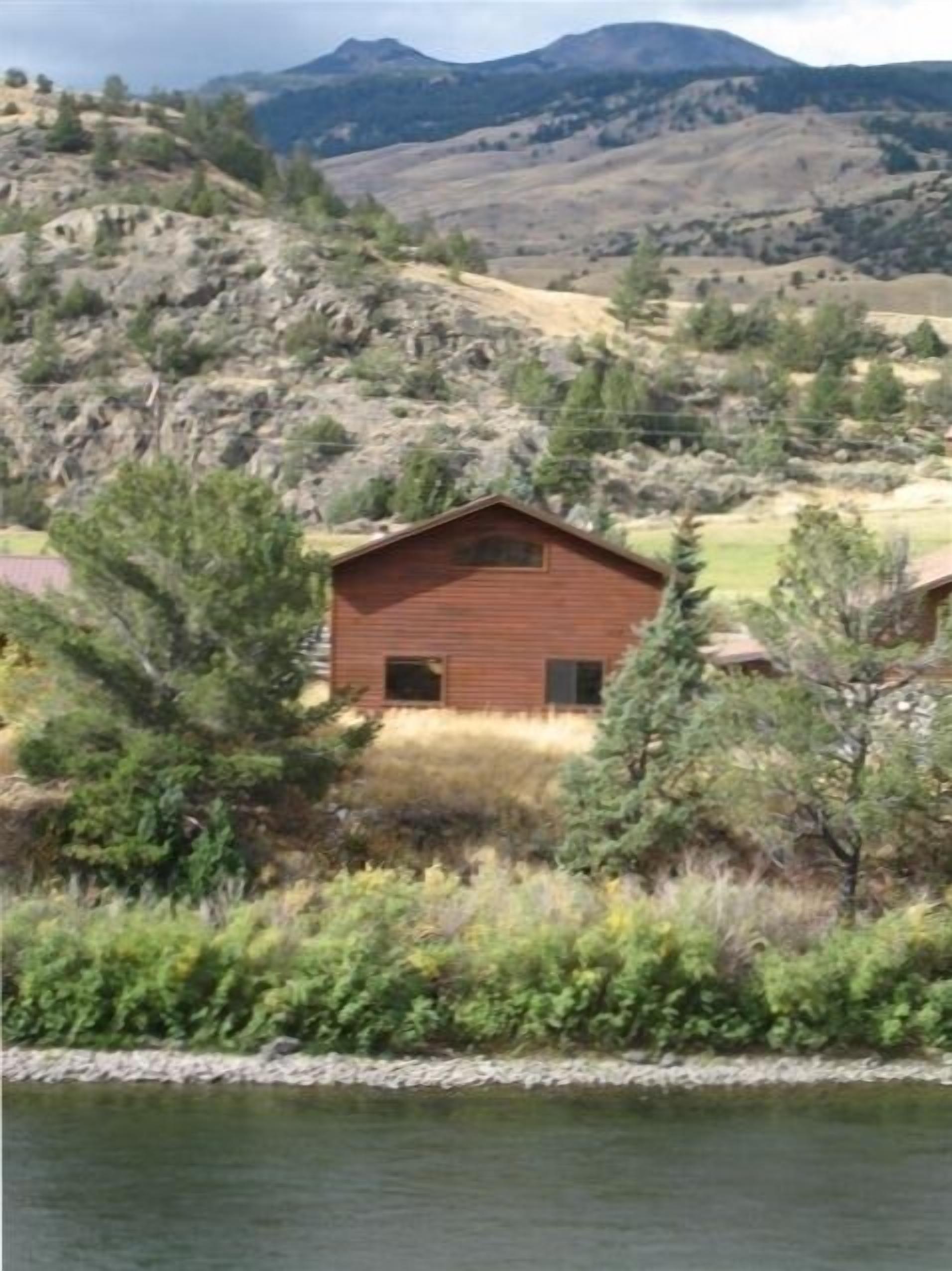 Una cabaña con techo inclinado, rodeada de abundante vegetación y un lago.