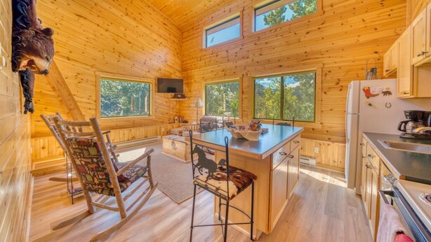 A cabin with wooden walls, a central island with seating, a kitchen area, and a bear decoration. - Horse Ranch on the Yellowstone River. Close to Gardiner and Yellowstone Park. (Emigrant)