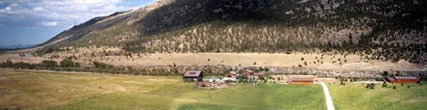 A rural landscape with a mountain, a field, and several buildings.