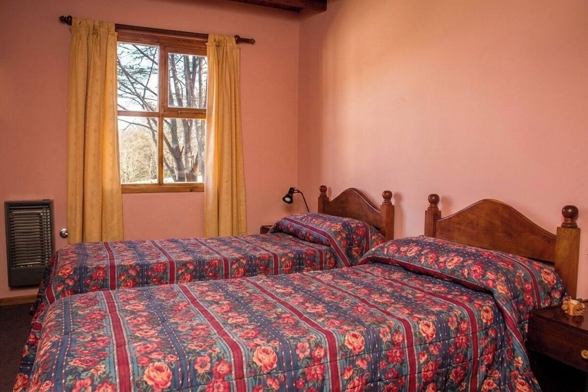 Une chambre avec deux lits, une fenêtre avec des rideaux et une table de chevet avec une lampe.