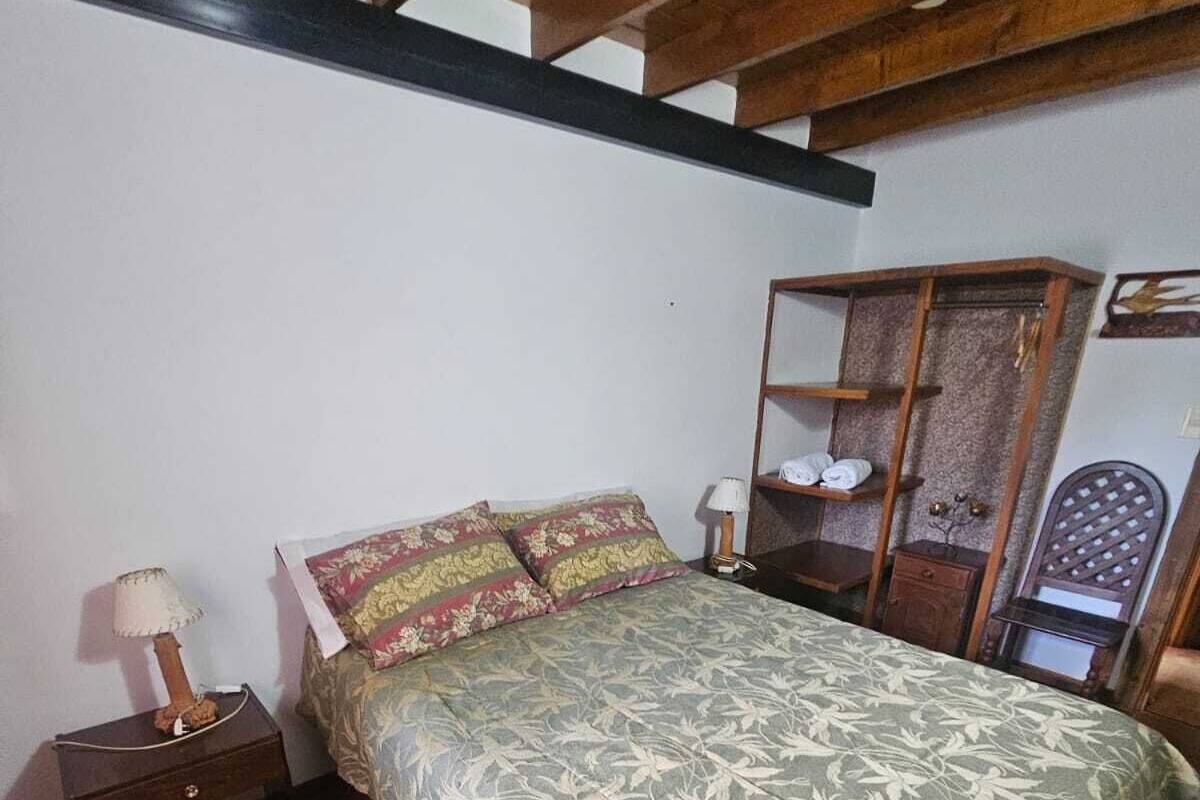 Une chambre à coucher comprenant un lit, une table de chevet, une armoire en bois et une chaise.