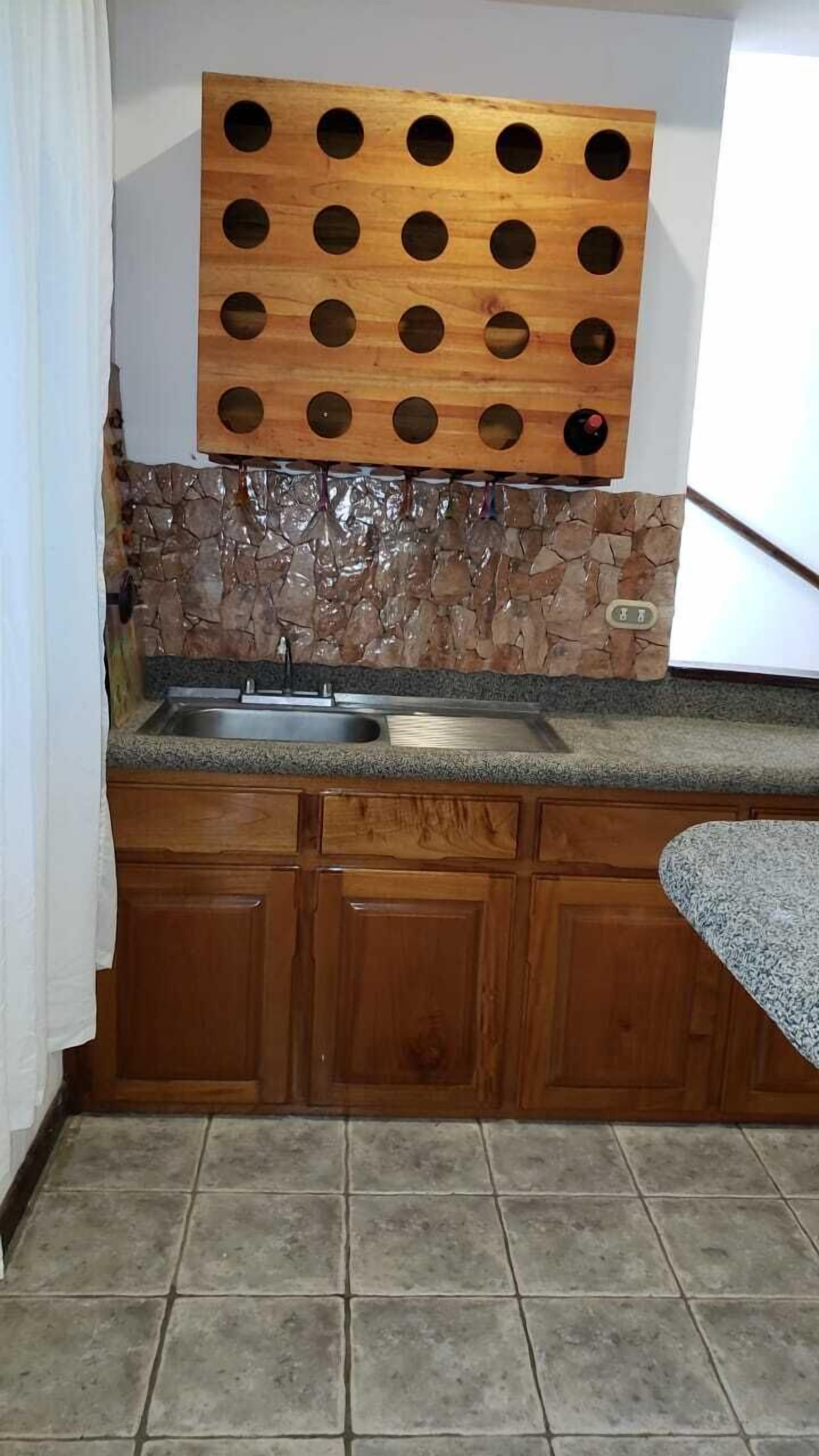 Une cuisine dotée d’un plan de travail en granit, de meubles en bois, d’un pare-feu en pierre et d’un panneau en bois avec des découpes circulaires au-dessus de l’évier.
