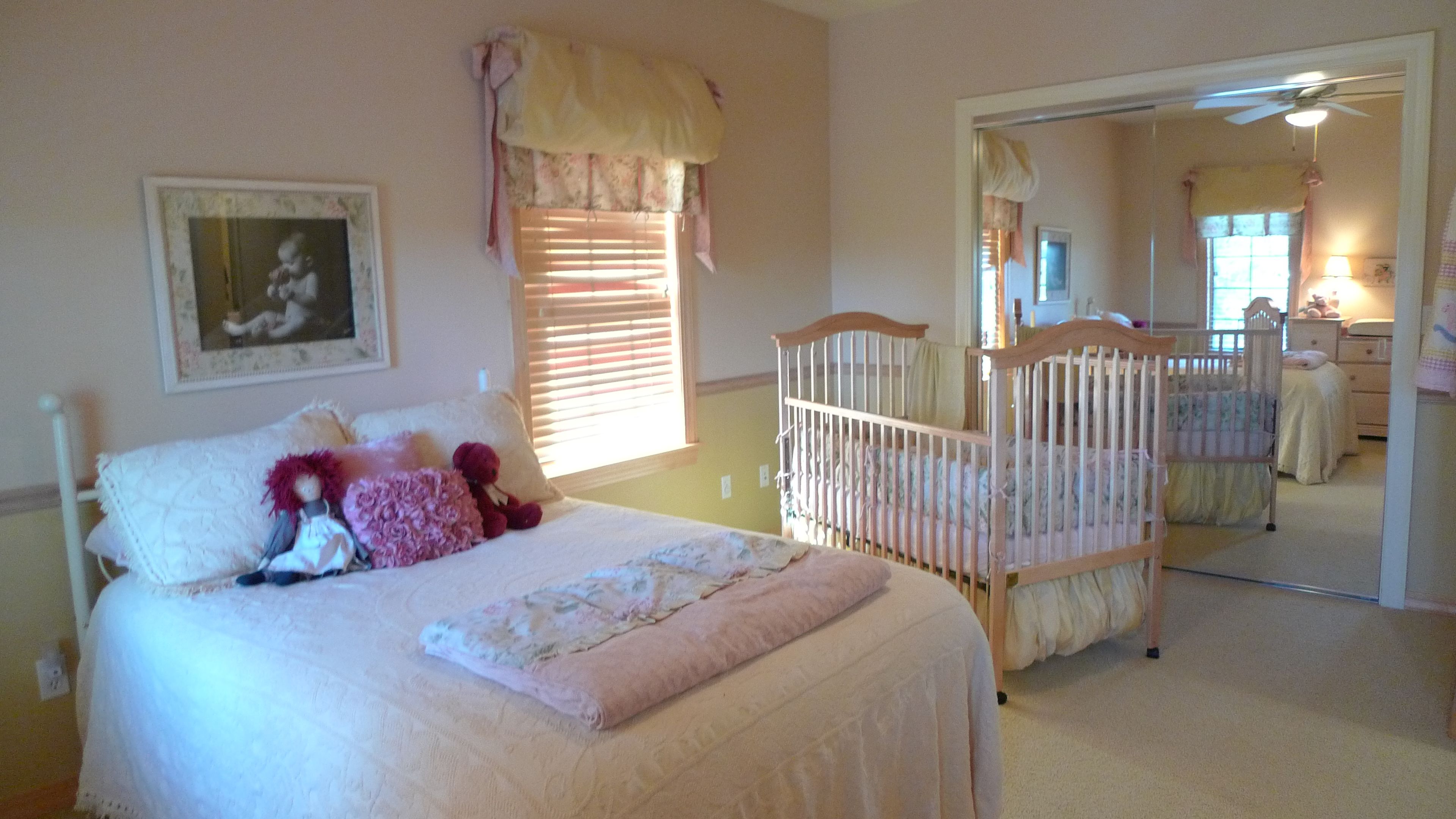 Una habitación infantil con una cuna, una cama con colcha, un espejo y un ventilador de techo.