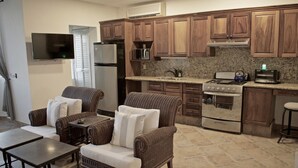 A kitchen with wooden cabinets, a built-in oven, a microwave, and a toaster. There is a dining area with wicker furniture and a TV mounted on the wall. - "Coral", One Bedroom Apartment. You can Walk to Beach and Restaurants.  (Punta de Mita)