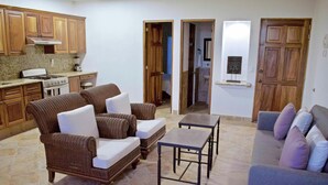 A living room with wicker furniture, a coffee table, and a sofa. There is a kitchen area with wooden cabinets and a stove. - "Coral", One Bedroom Apartment. You can Walk to Beach and Restaurants.  (Punta de Mita)