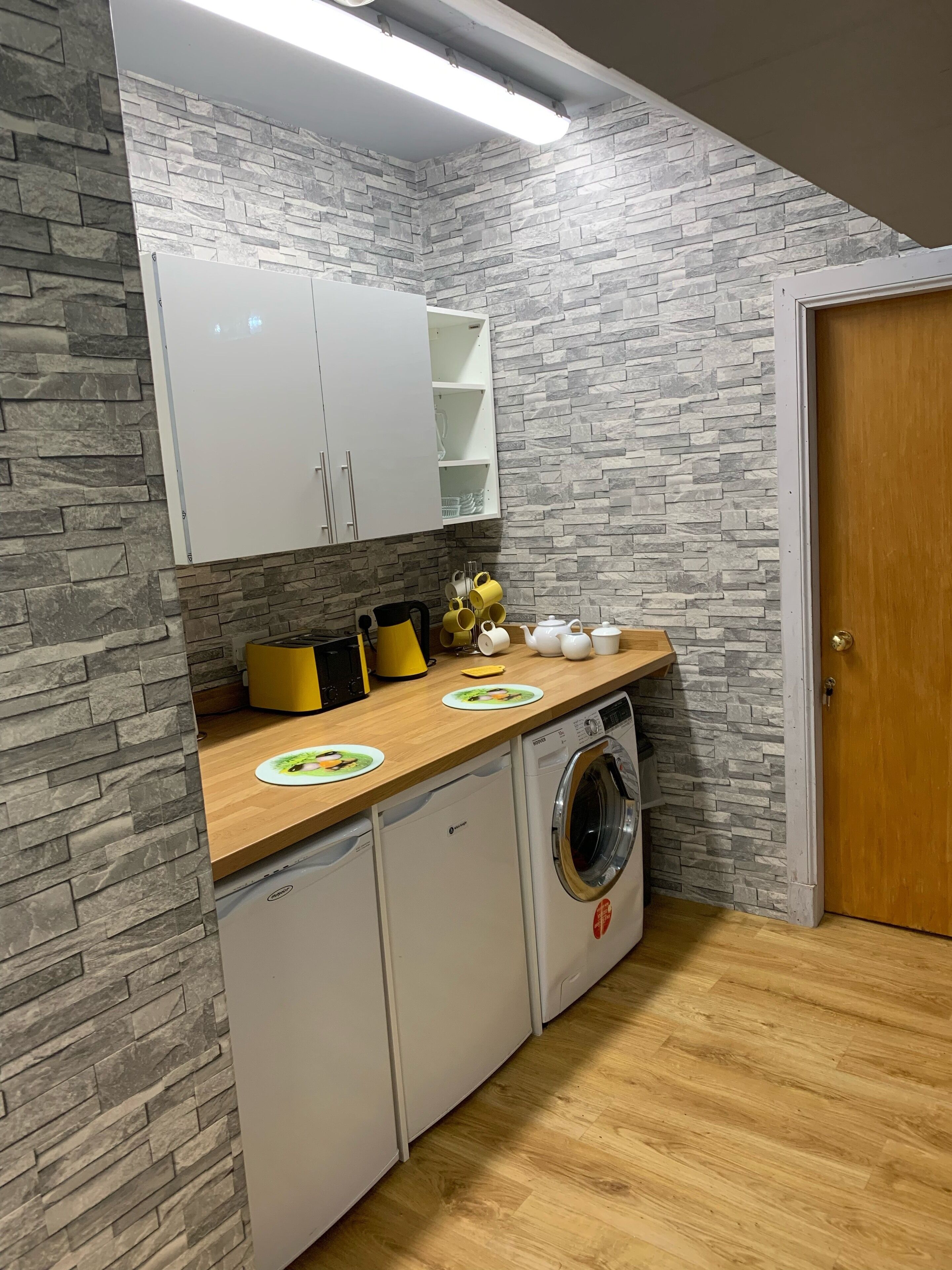 Eine kleine Küche mit einer Rückwand im Stein-Look, weißen Schränken, einer Waschmaschine und einer Holz Arbeitsplatte.