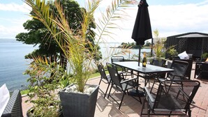 Une terrasse extérieure aménagée avec des meubles en osier, une table et des chaises, et une vue sur la mer.