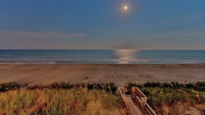 A beach with a wooden boardwalk leading to the water, a clear sky, and a visible moon.
