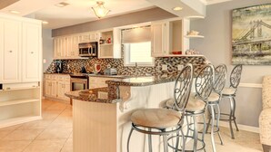A kitchen with white cabinets, a granite countertop, and a bar area with metal chairs.