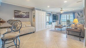 A spacious living area with a dining table, two sofas, and a coffee table. There is a large window with a view of the ocean.