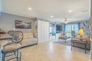 A spacious living area with a dining table, two sofas, and a coffee table. There is a large window with a view of the ocean.