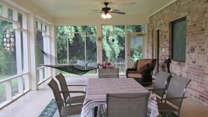 A covered patio with a table, chairs, a hammock, and a ceiling fan.