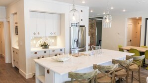 A modern kitchen with white cabinetry, a large island, and wooden chairs.