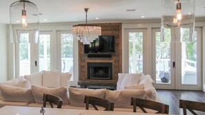 A modern living room with a fireplace, white sofas, a dining table, and pendant lights.