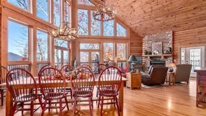 A spacious cabin with a large dining area, wooden walls, and a stone fireplace. - Serenity Retreat (Formerly Leins Lodge) Luxury Home Stunning Mountain Views (Maggie Valley)
