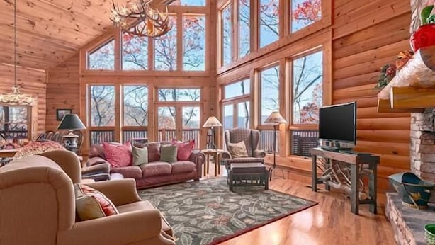 A cozy log cabin interior with a large window, a fireplace, a television, and a comfortable seating area. - Serenity Retreat (Formerly Leins Lodge) Luxury Home Stunning Mountain Views (Maggie Valley)