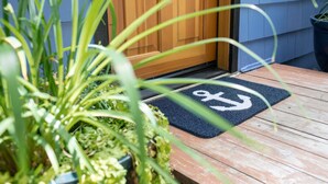 Une porte en bois surmontée d’un paillasson noir orné d’un symbole d’ancre.