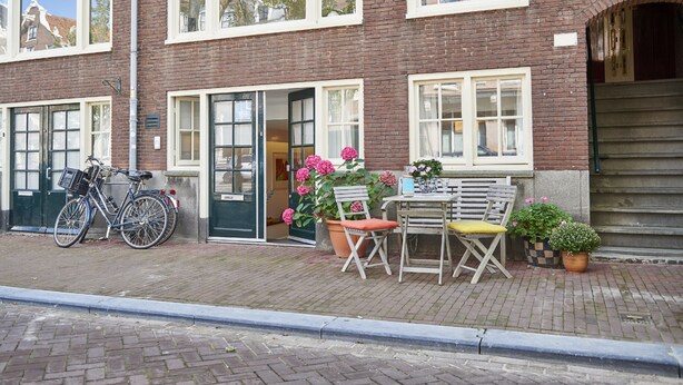 A brick building with a bicycle parked outside, a table with chairs, and potted plants.