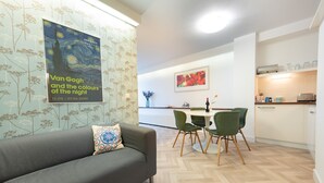 A modern living room with a grey sofa, a dining area with a table and chairs, and a kitchen in the background.