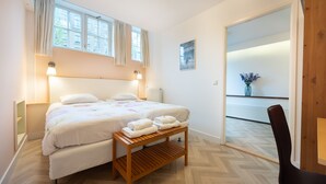 A bedroom with a double bed, a wooden bench with towels, a nightstand, and a view of a balcony with a vase of flowers.