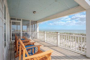 Une terrasse couverte, dotée de bancs en bois et d’une balustrade, qui offre une vue sur la plage.