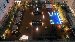 An outdoor pool area with seating and plants, surrounded by a building with multiple windows. - Oriental Hotel Fukuoka Hakata Station (Fukuoka)