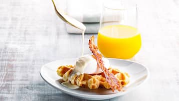 Un plato con waffles, una bola de helado y una loncha de tocino. Se ve un vaso de jugo de naranja al fondo.