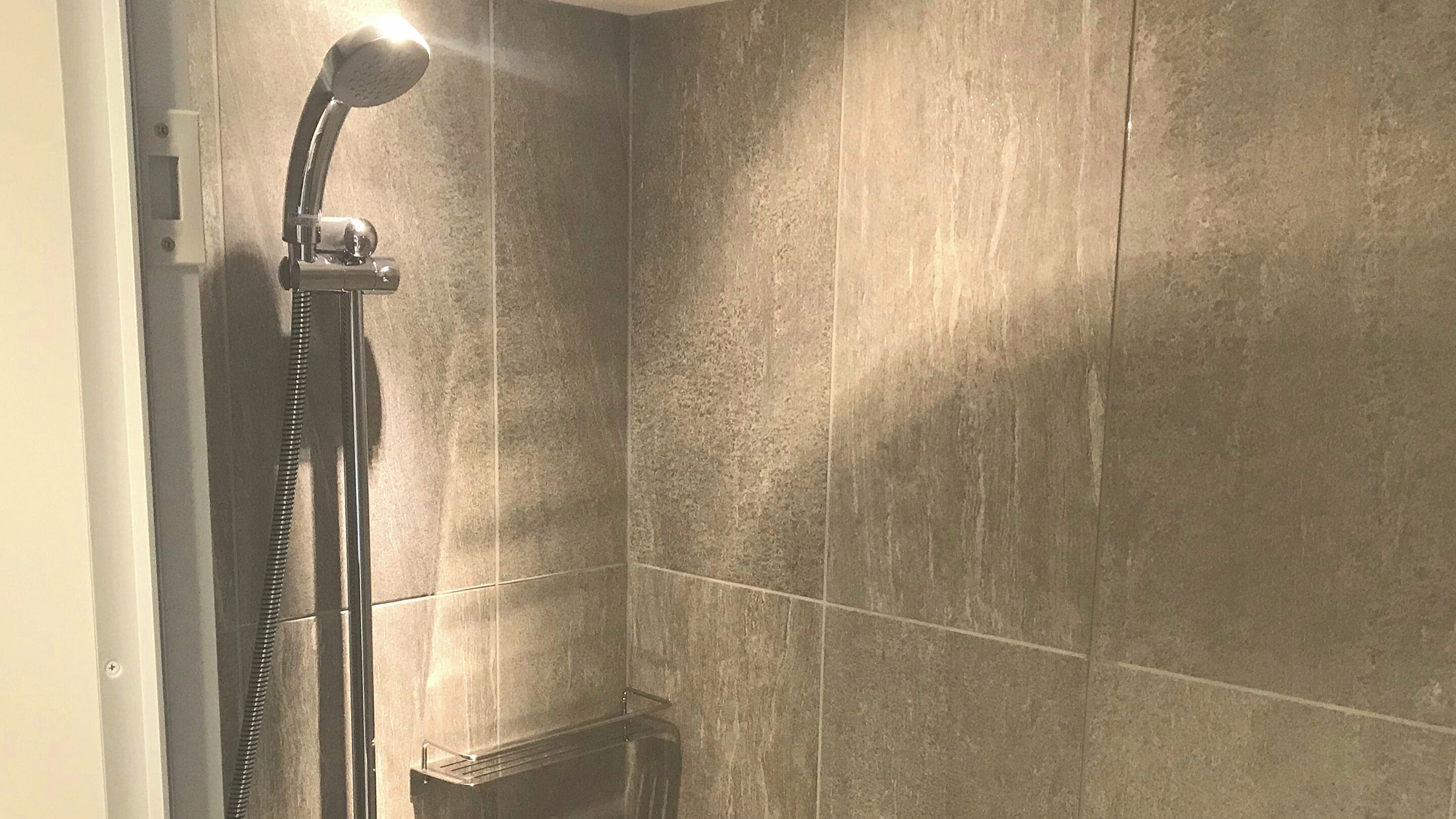 Une douche équipée d’un pommeau de douche à main et d’un panneau de commande fixé au mur.