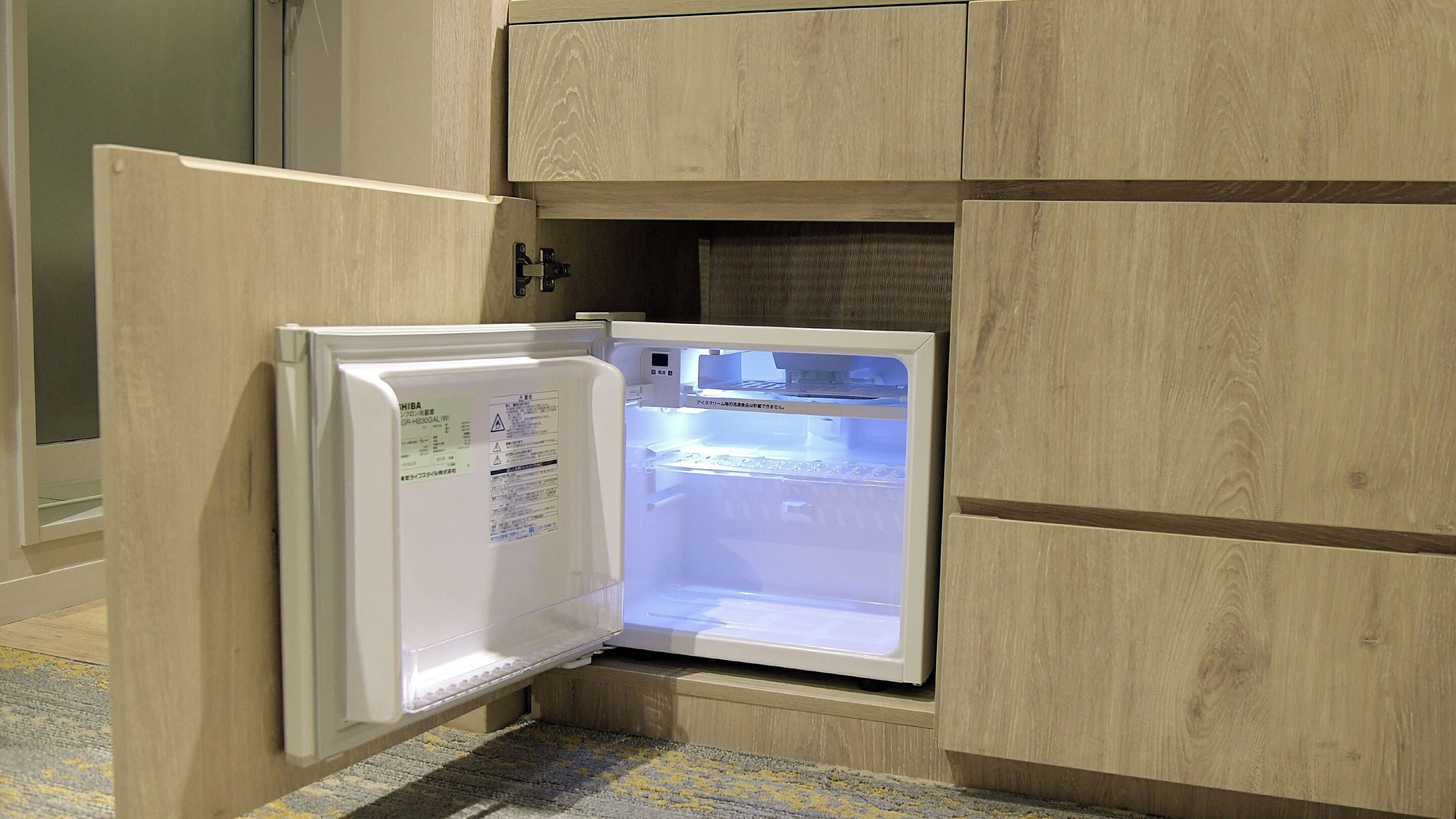 A compact refrigerator with a digital display, situated in a kitchen with wooden cabinetry.