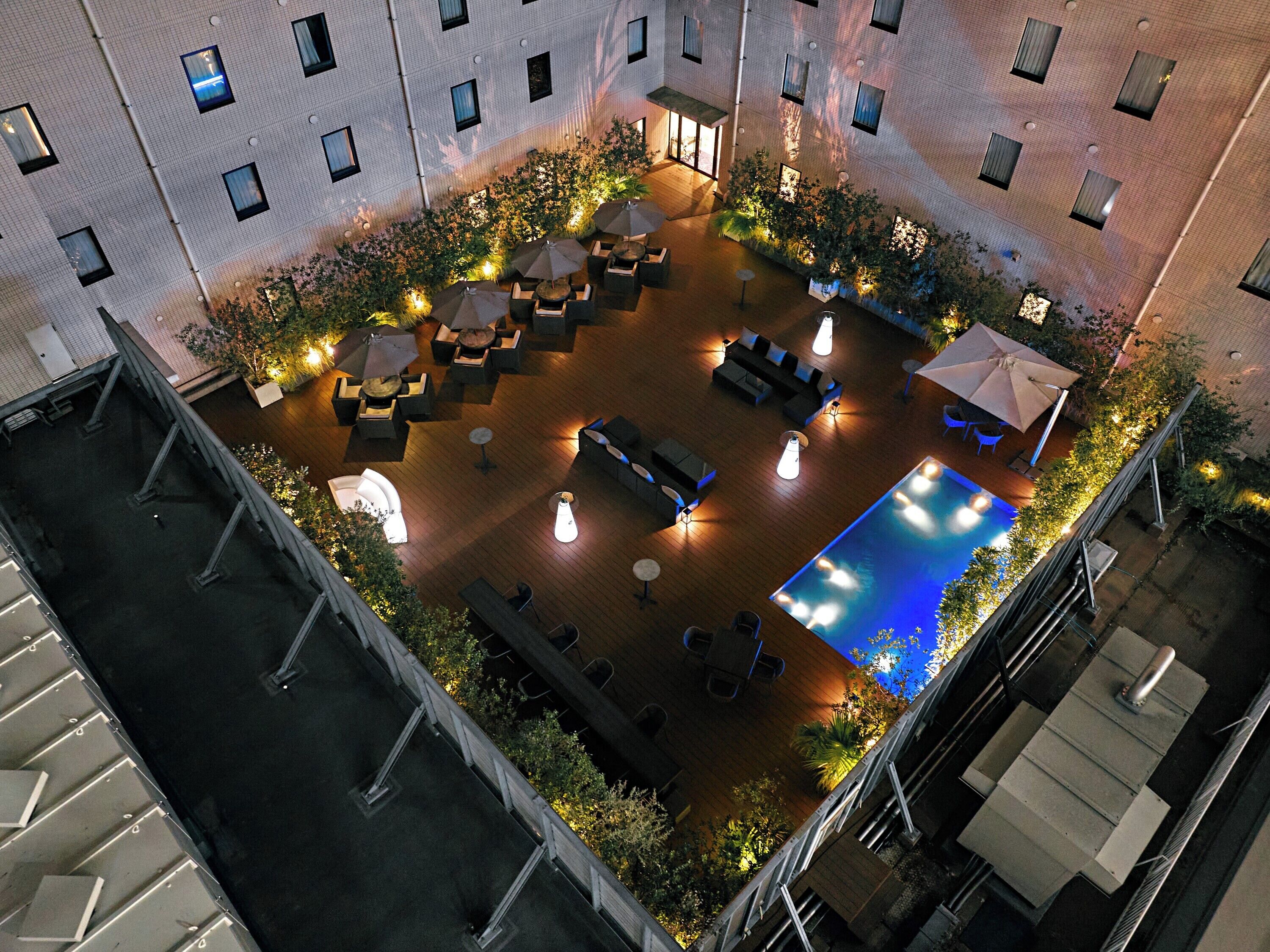 An aerial view of a rooftop patio with a pool, outdoor seating, and greenery.