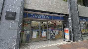 Un negozio di alimentari Lawson con insegna blu, vetrine e uno sportello bancomat ben visibile.