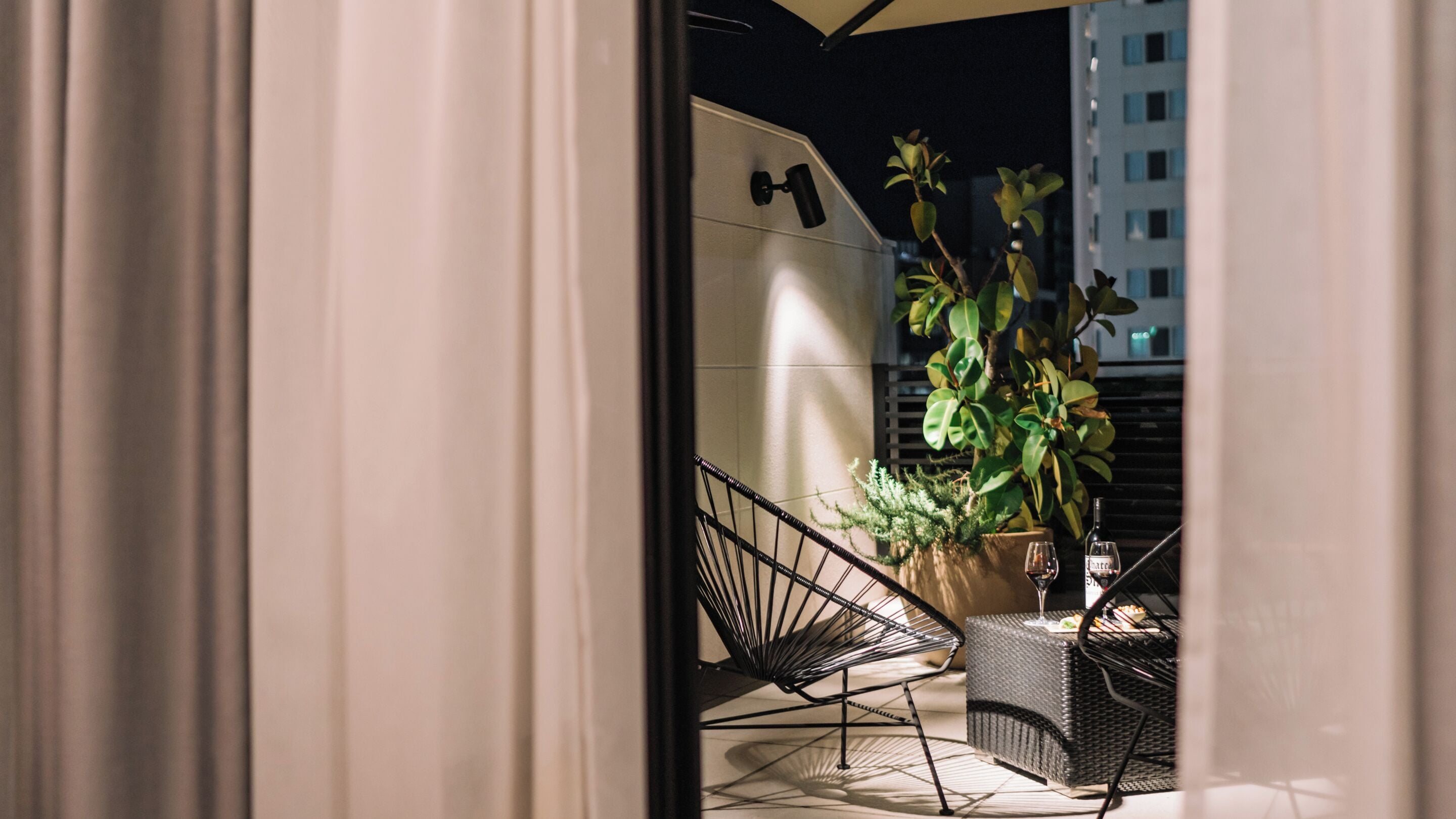 A balcony with a wicker table, chairs, and a potted plant.