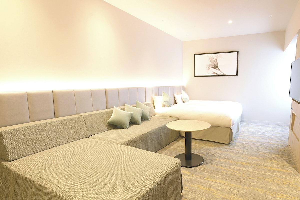 A modern hotel room with a sofa, a small round table, a bed, and a TV.