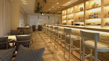 A bar area with a long counter, multiple bar stools, and shelves with bottles and glasses.