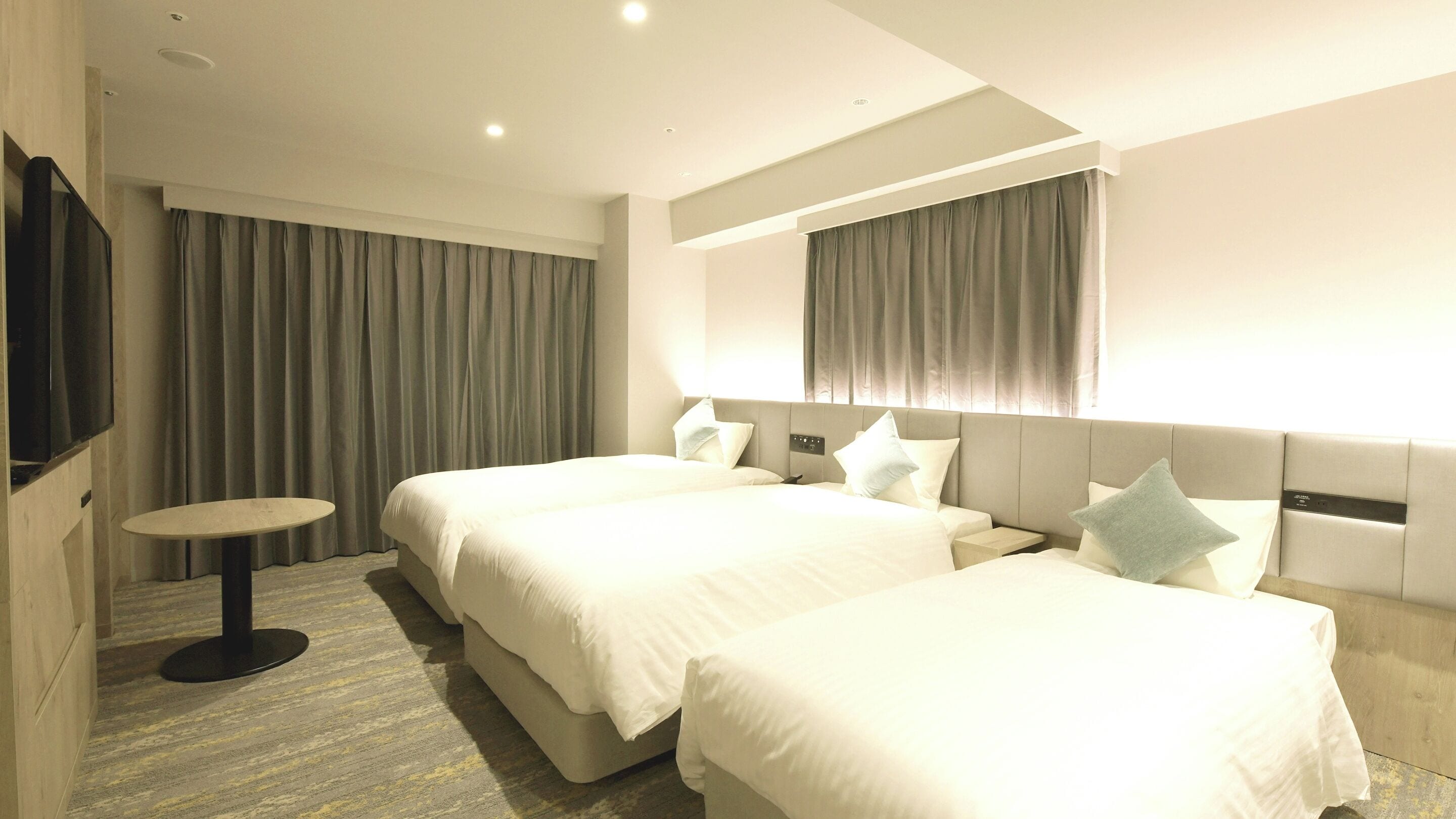 A hotel room with two beds, a small round table, and a TV on the wall.