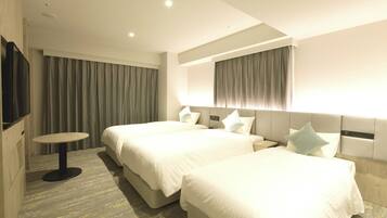A hotel room with two beds, a small round table, and a TV on the wall.