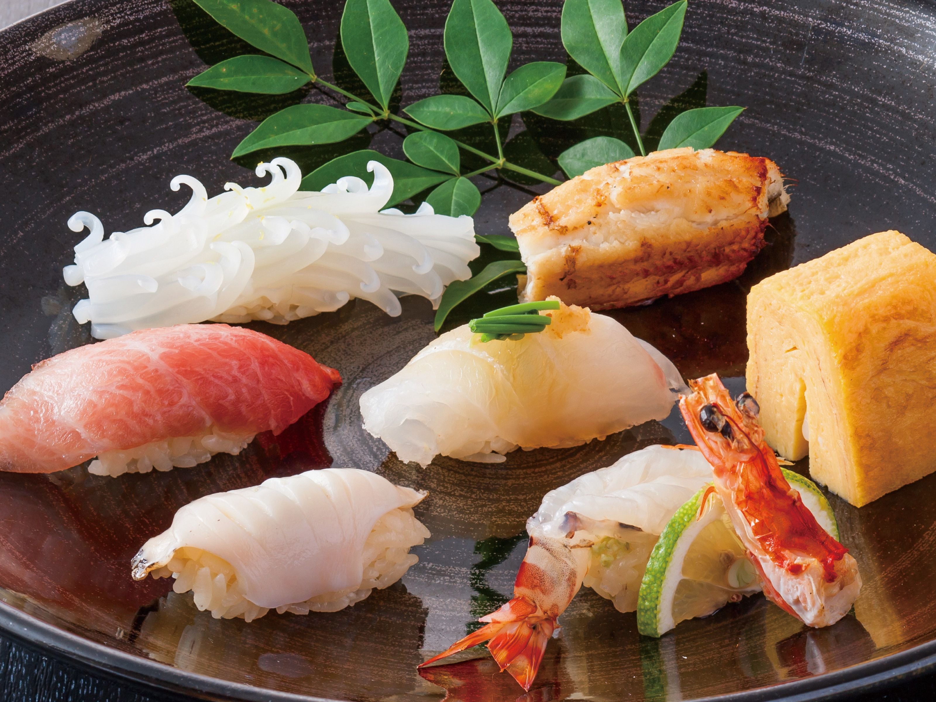 Diverse soorten sushi op een zwart bord, waaronder zalm, tonijn en garnaal.