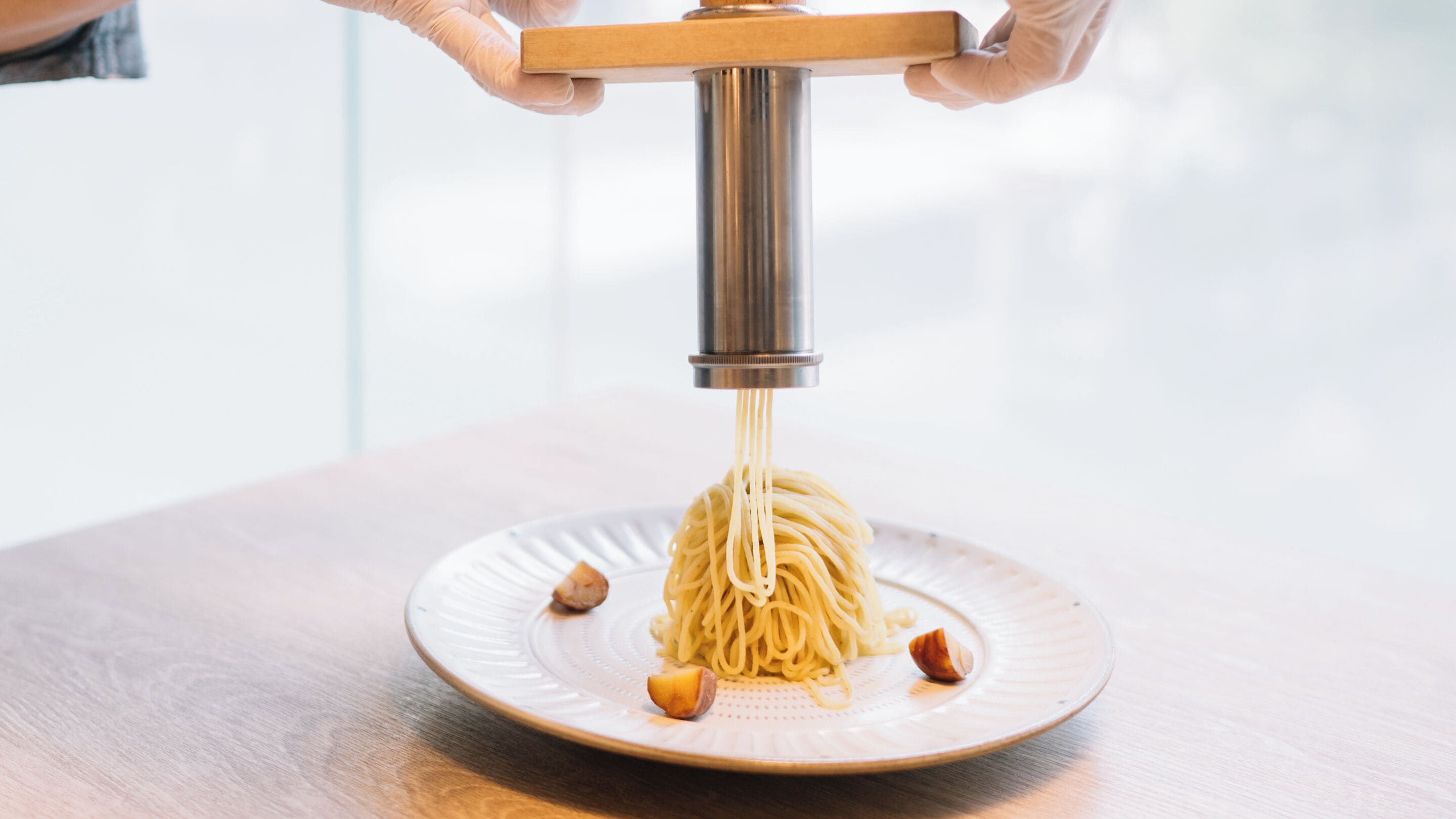 Une personne utilise une machine à pâtes pour préparer des spaghettis qu'elle dispose ensuite dans une assiette.
