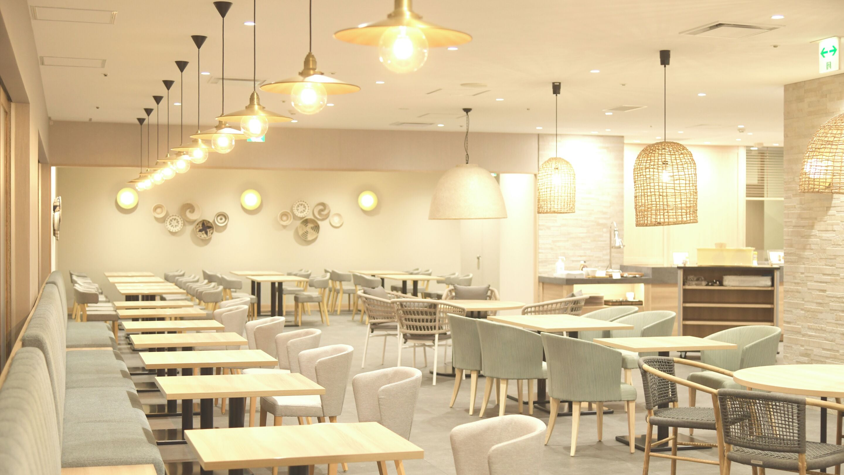 A modern restaurant with long communal tables and booths, pendant lighting, and decorative wall plates.