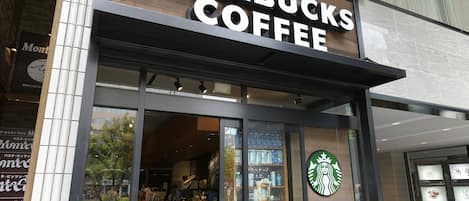 Una tienda Starbucks Coffee con fachada moderna, grandes ventanales de vidrio y un interior visible con estantes llenos de productos.