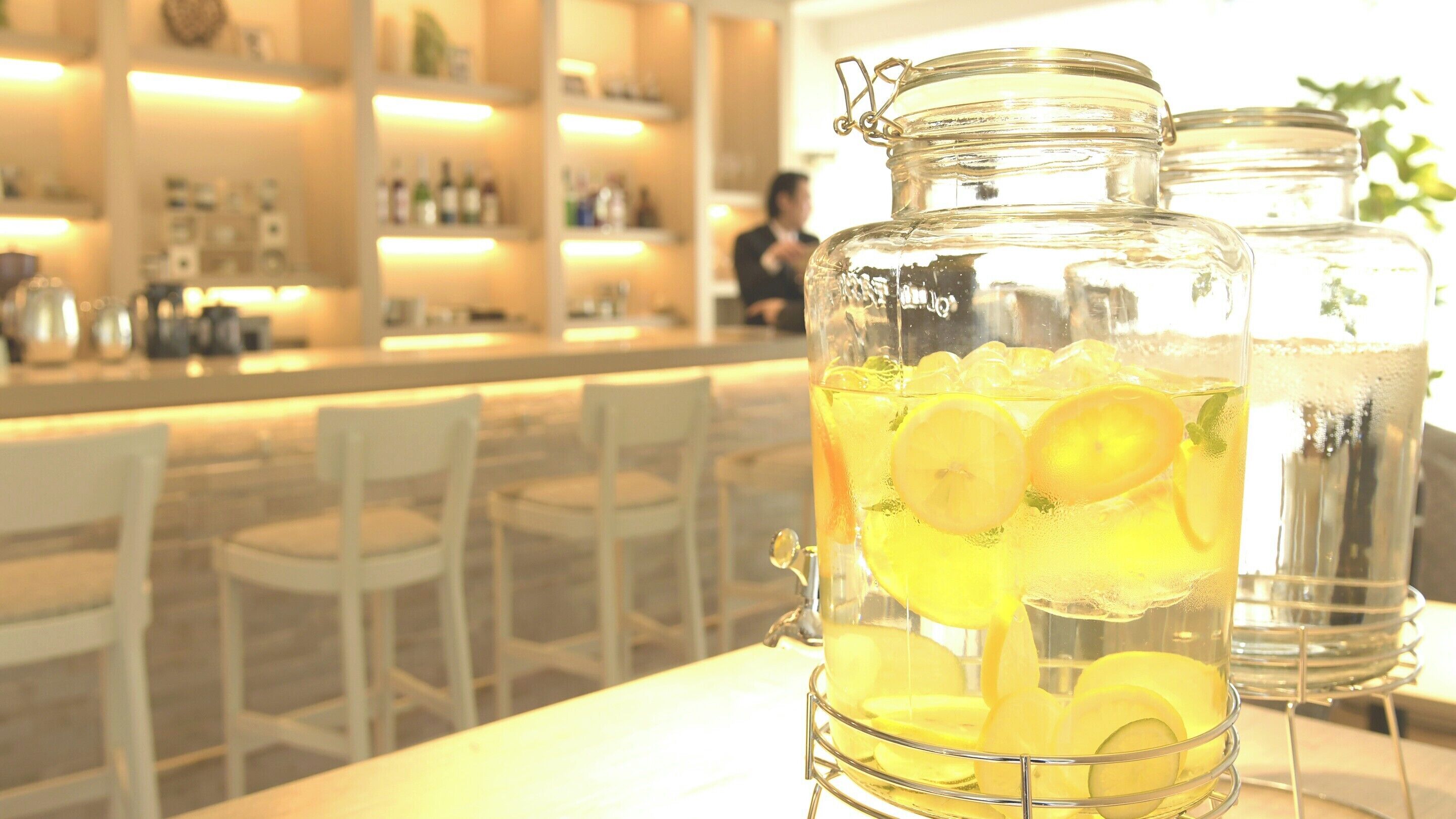 Un área de bar con una jarra grande de vidrio llena de una bebida amarilla, hielo y rodajas de limón.