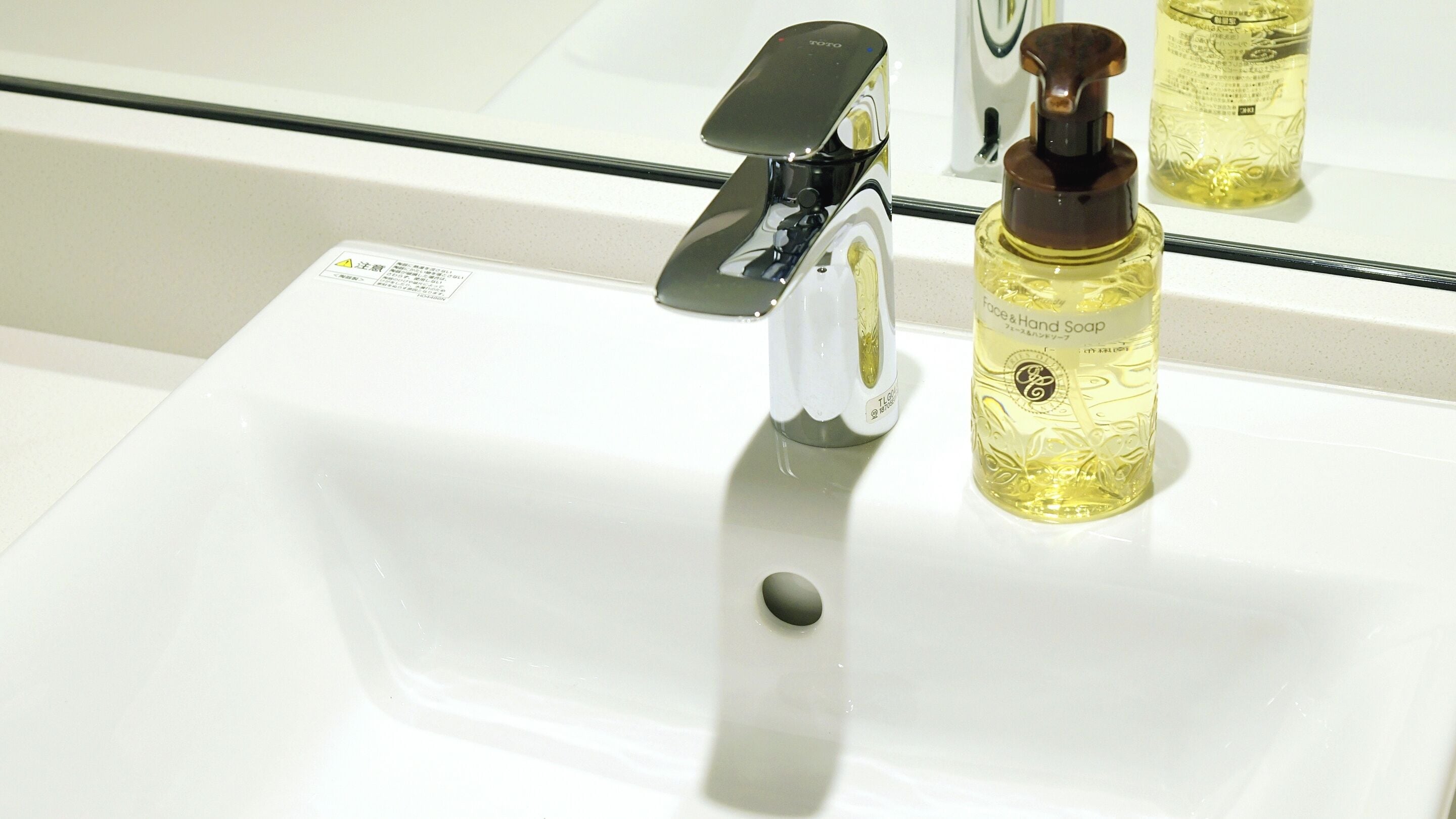 A bathroom sink with a faucet and a bottle of face and hand soap.