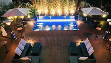 Une piscine entourée de plantes et dotée d’une terrasse en briques, avec des chaises longues et des parasols.