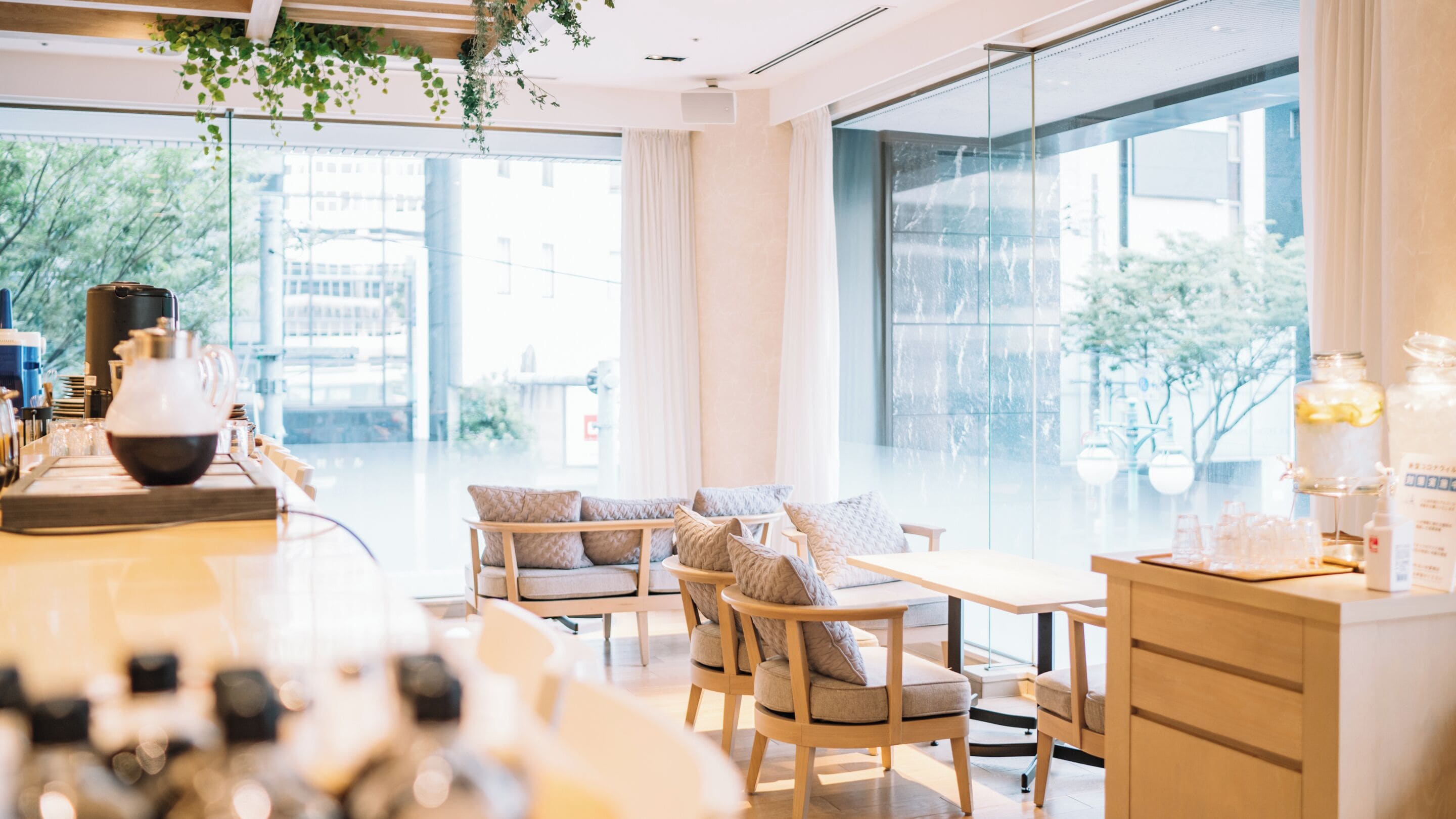 A modern cafe with a large window, wooden furniture, and a coffee station.
